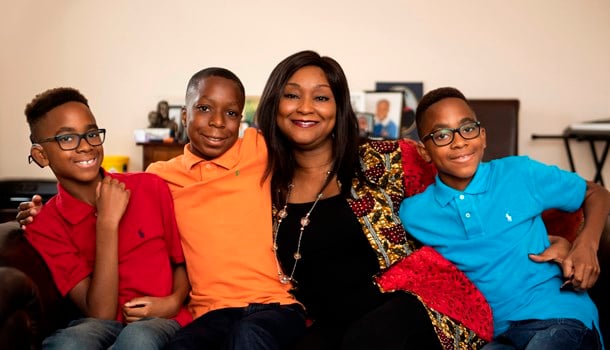 Oyin, a black woman, sits on the sofa surrounded by her three sons.