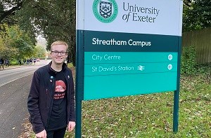 Daniel (18) standing in front of a sign for the University of Exeter
