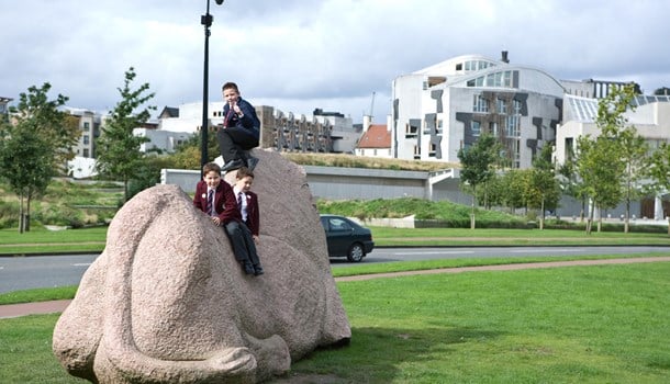School children sitting on top of a statue in a grassy area