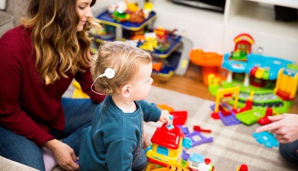 A baby with a white cochlear implant and her mum playing with toys on the floor.