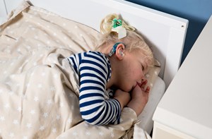 A young girl wearing hearing aids sucking her thumb while laid in bed. 