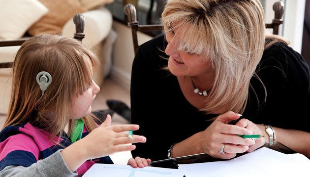 A woman helps a girl wearing cochlear implants with school work.