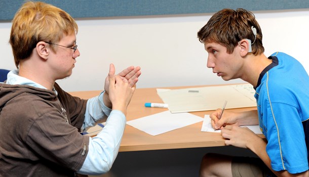 A teenager signs to his friend who wears a cochlear implant.