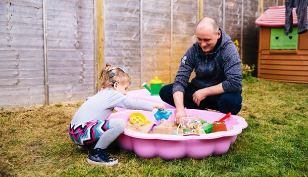 Lily wearing her cochlear implants and playing in a sandbox with her dad.