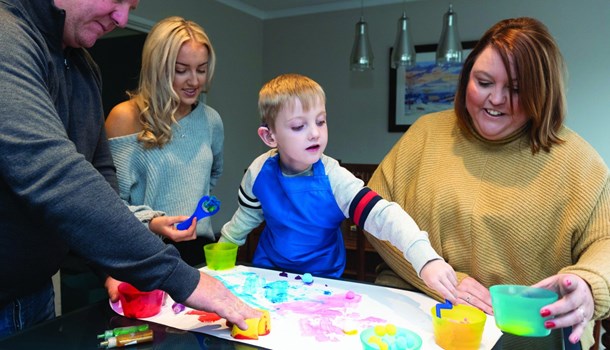 A deaf young boy painting with his parents and older sister.
