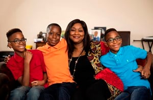 Oyin, a black woman, sits on the sofa surrounded by her three sons.