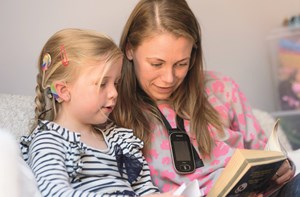 A young girl with a cochlear implant reading with her mum who's wearing a radio aid.