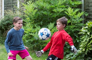 A deaf boy with cochlear implants playing football with his brother in their garden.