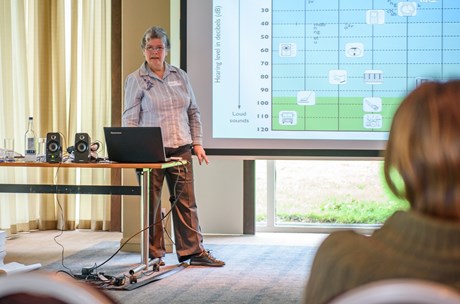 A person standing in front of a presentation, presenting to an audience of adults.