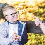 Xander wearing cochlear implants and glasses signing with his mum on a park bench.