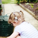 A young girl with glasses, plaits and an auditory brainstem implant (ABI) kneeling down.