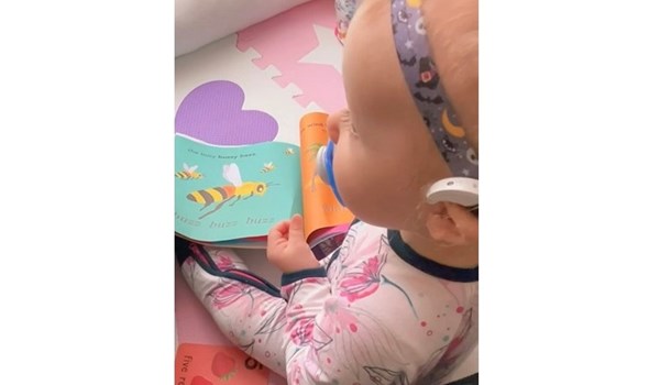 Baby girl wearing hearing aids and reading 'Ling Ling Bird' book