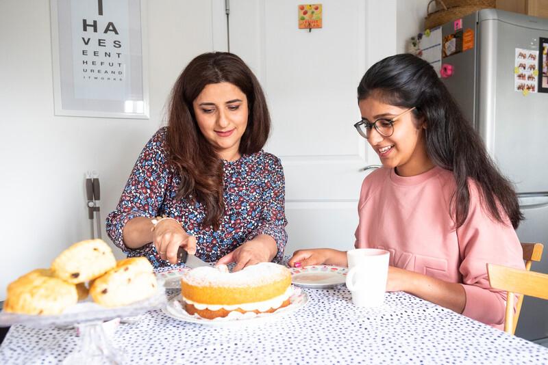 Two smiling women cutting a cake 