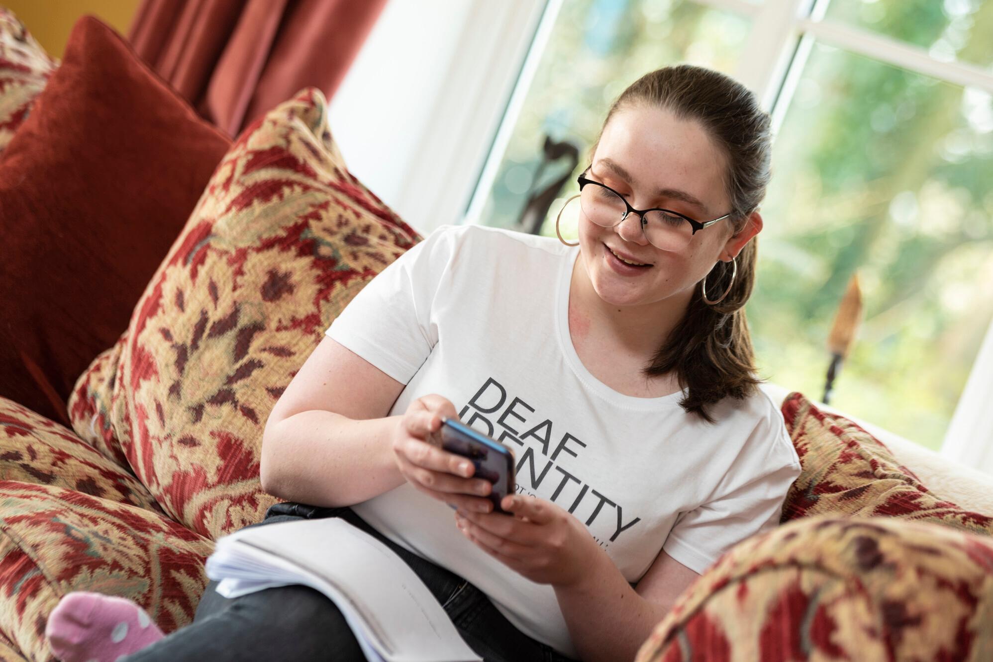 Teenage girl sat on sofa wearing T-shirt that reads 'Deaf identity'