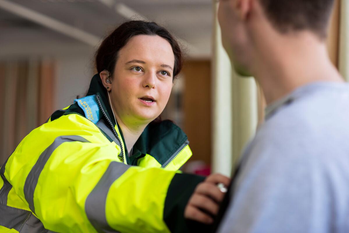 Holly wearing a high-visibility paramedic coat while using a stethoscope on a patient.