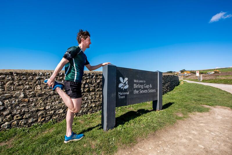 A man dressed in running gear stretching in a country park 