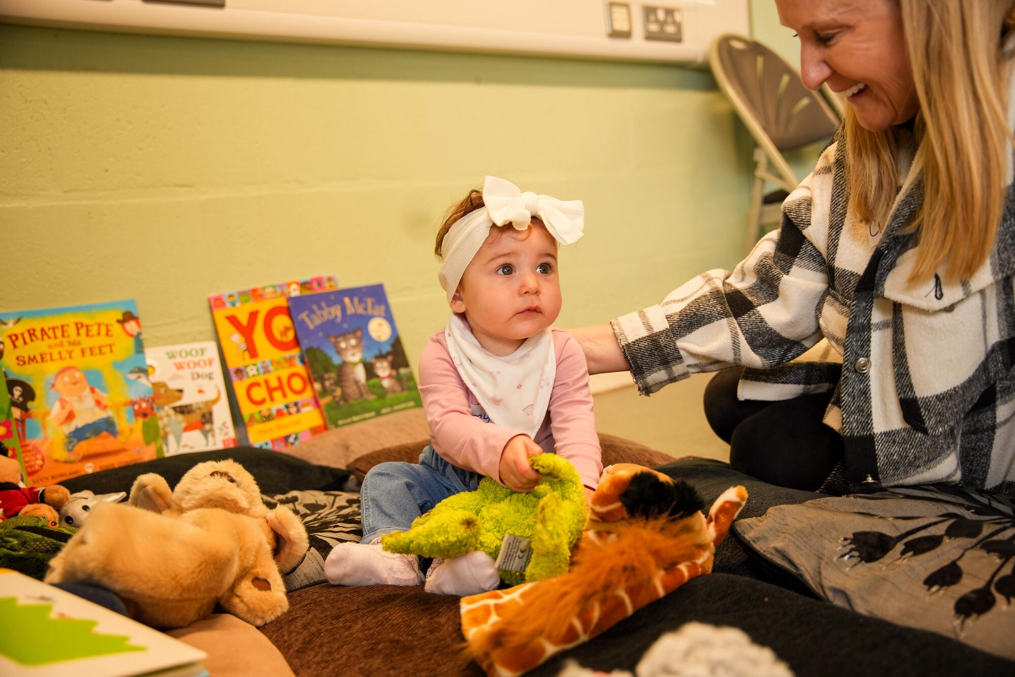 An early years practitioner playing with a toddler on the floor