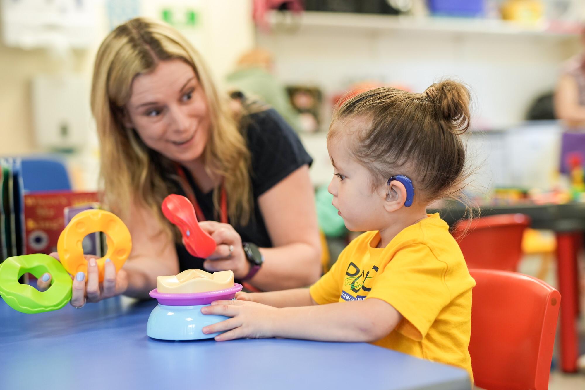 An early years practitioner playing with a toddler in a school setting