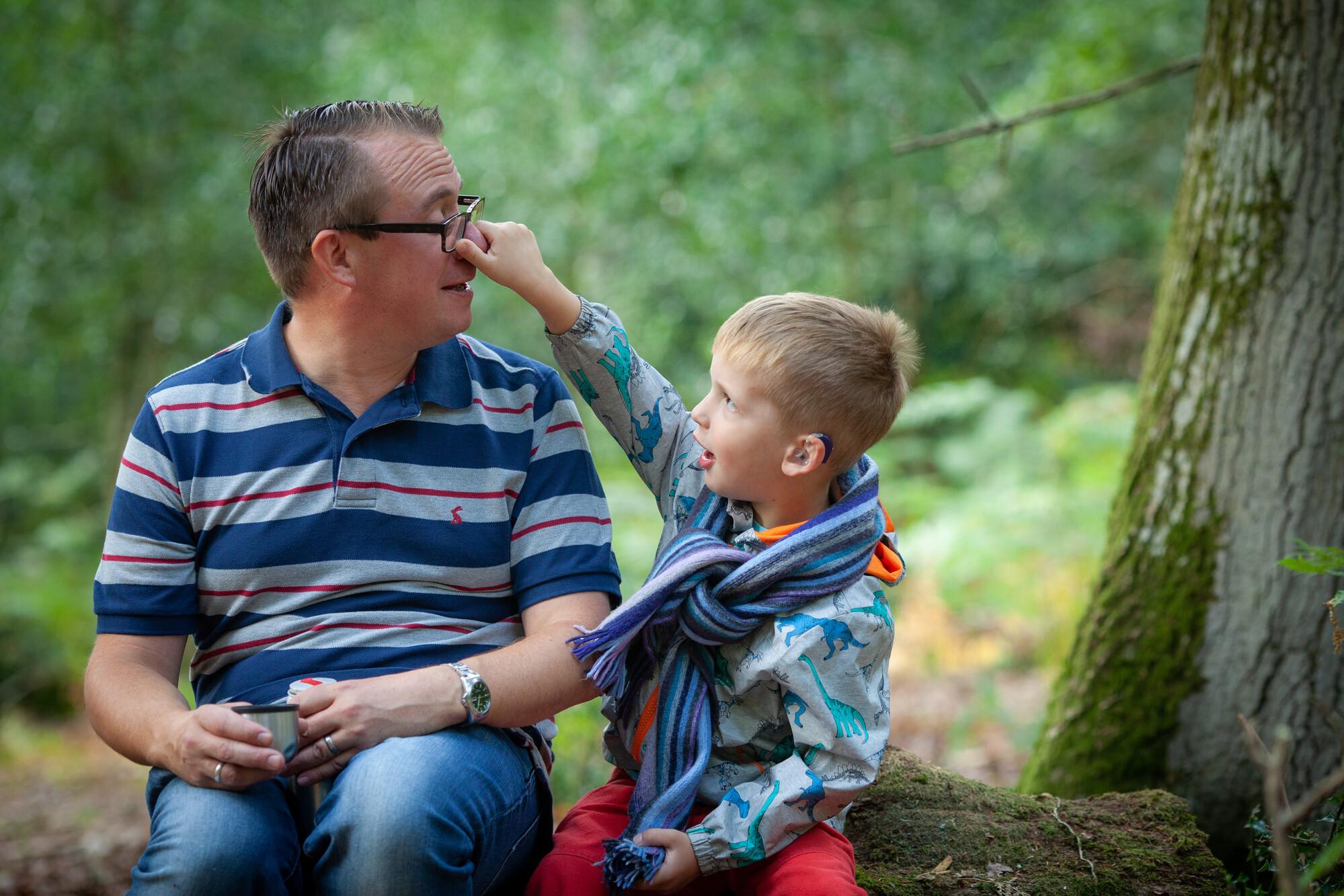 A dad and his son sitting on a log in a forest together
