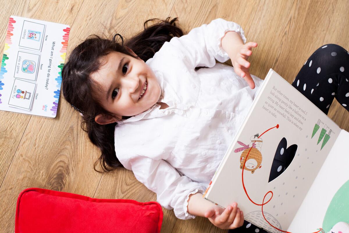 Holi laid on the floor, smiling at the camera and holding a book.