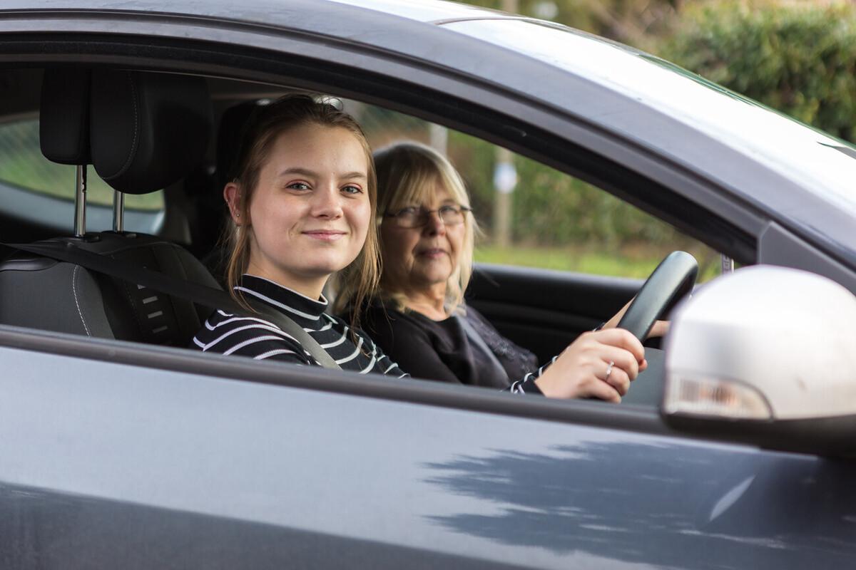 Megan sat in the car with her mum - they're both looking out of the open window at the camera.