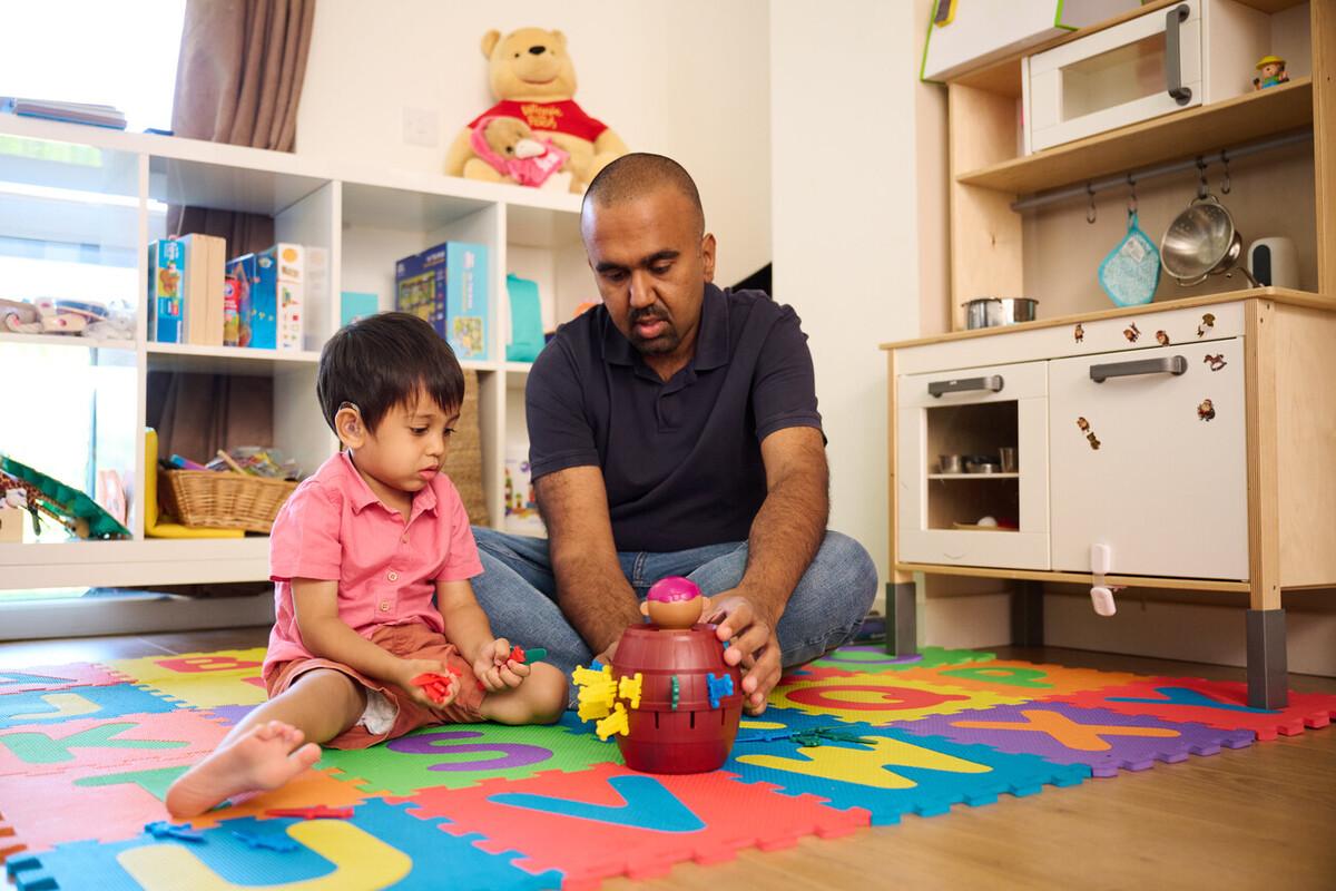 A young child with a hearing aid plays a game with an adult male