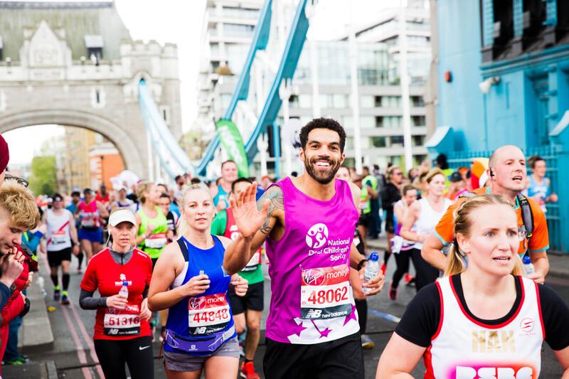 People running the London marathon smiling on London bridge