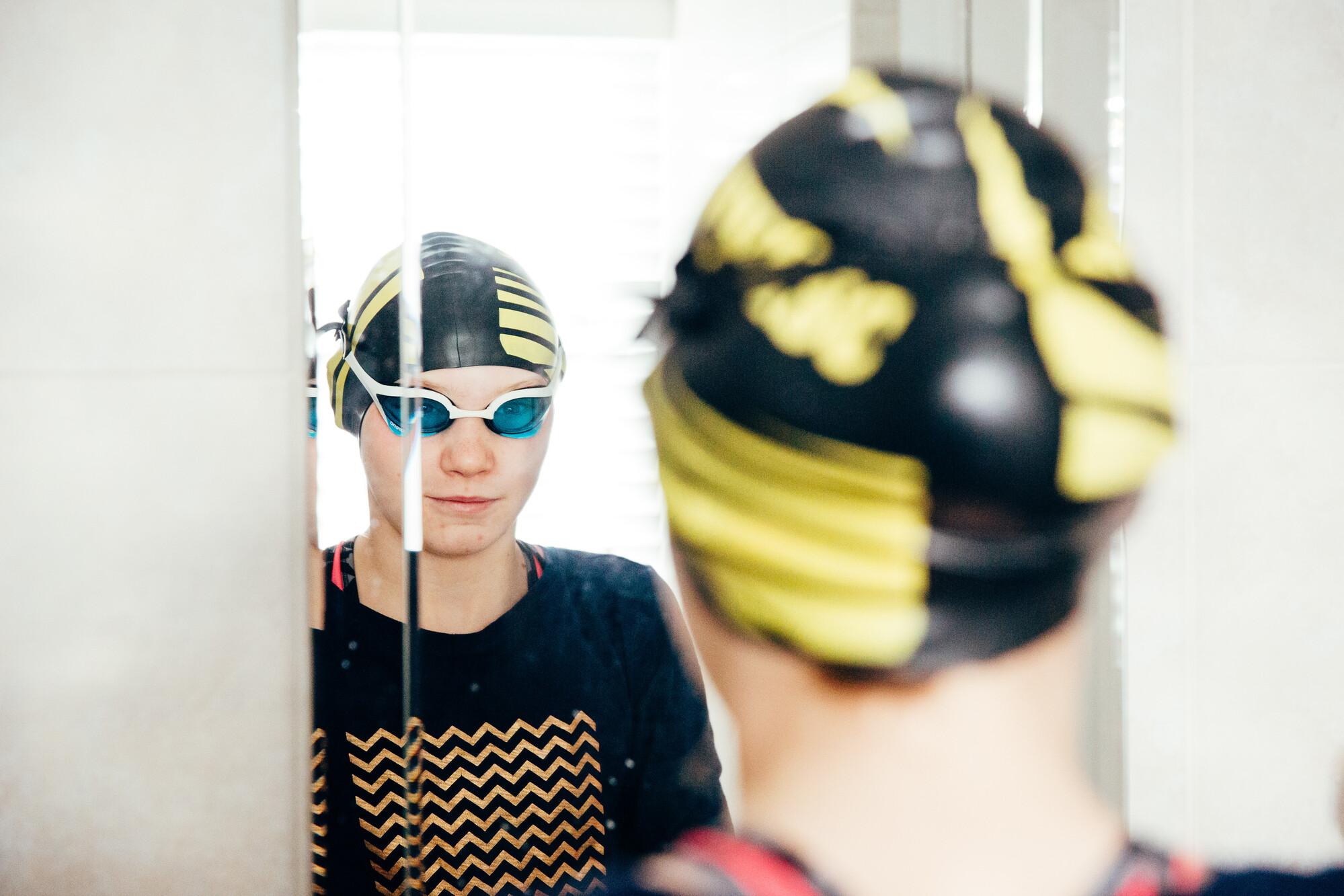 A person stood looking in the mirror wearing a swimming cap and goggles