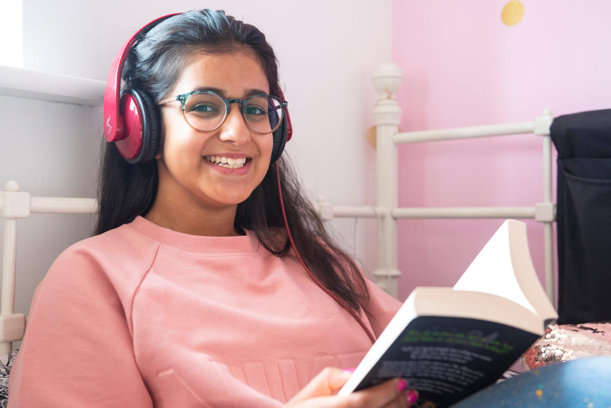 Teenage girl wearing pink over-the-ear headphones while reading a book