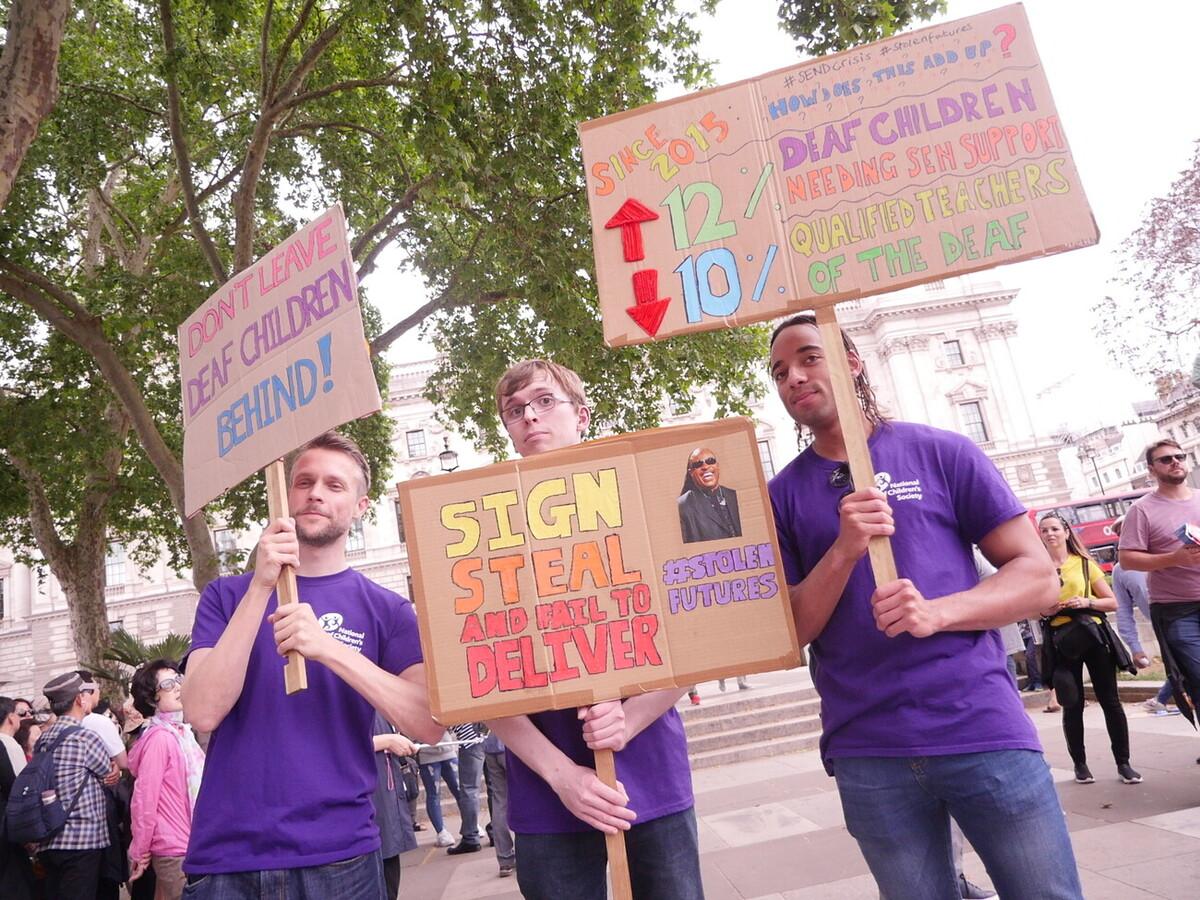 Three men hold campaigning placards.