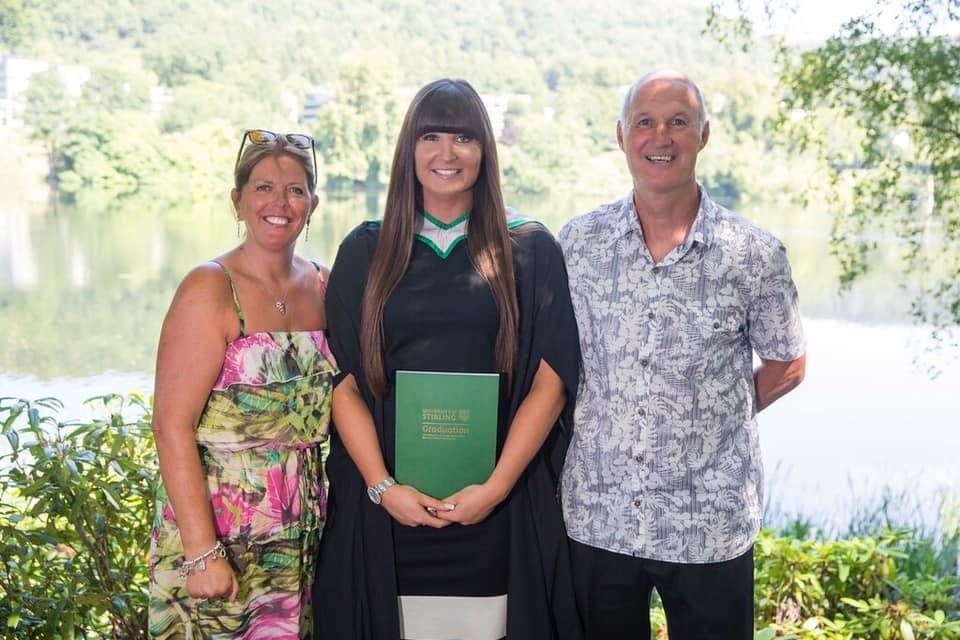 Young woman in graduation gown standing next to parents
