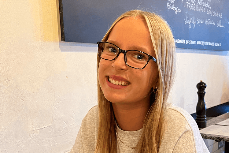 Headshot of a girl with blonde hair and glasses looking at the camera and smiling