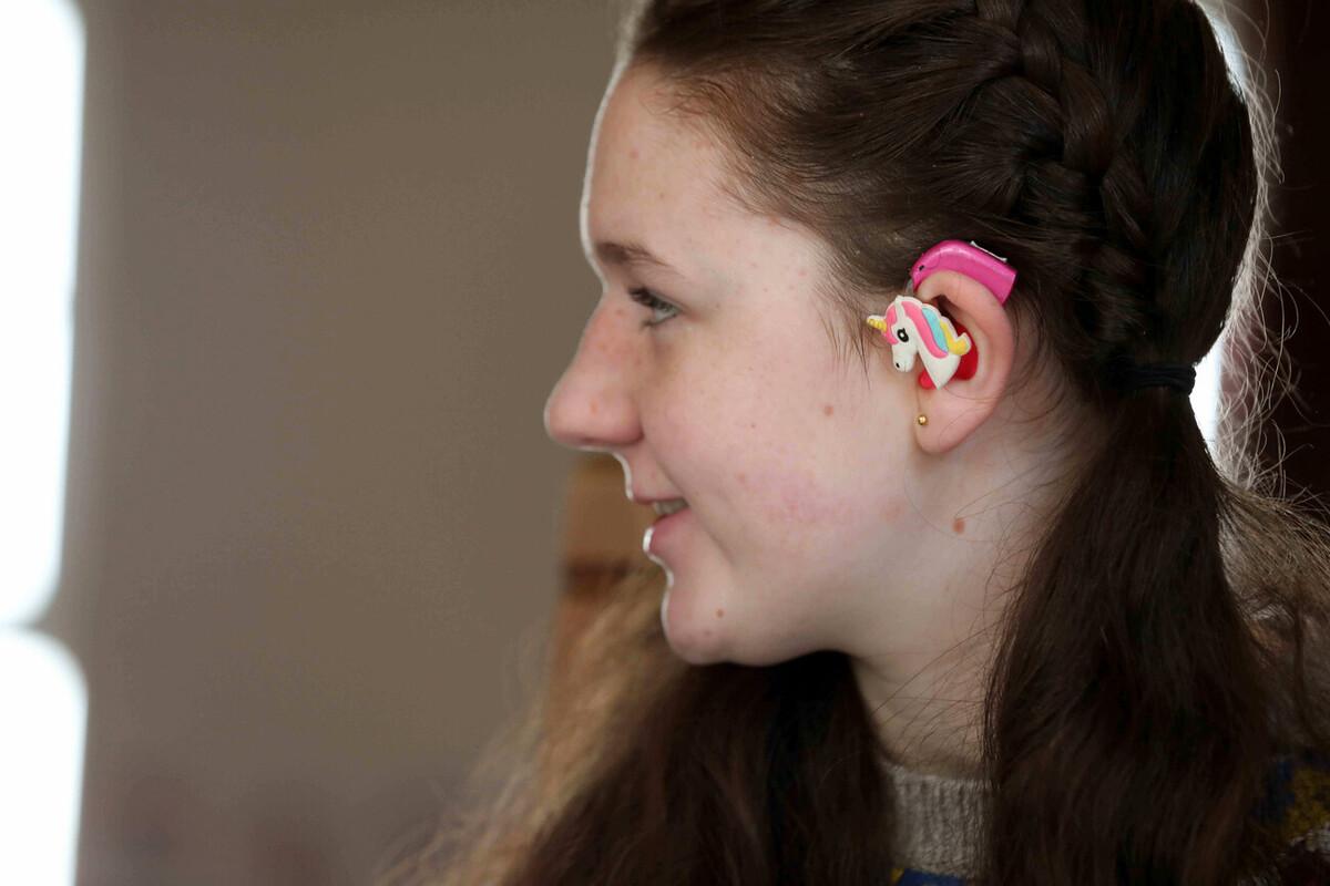 Teenage girl wearing a pink hearing aid with a unicorn clip