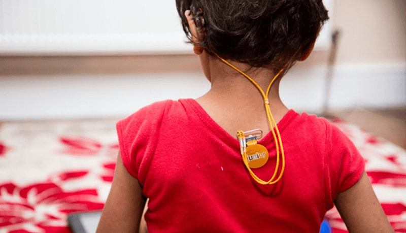 A clip attached to the back of a child's shirt with a cord securing her two hearing aids