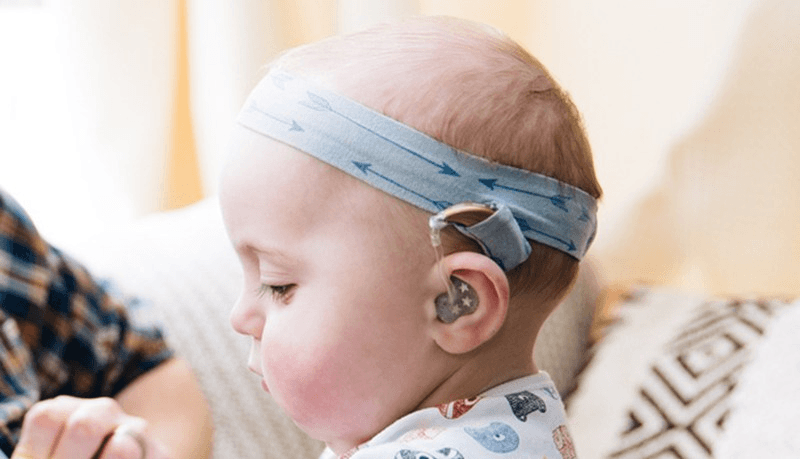 Baby wearing a headband with a secure pocket for her hearing aid