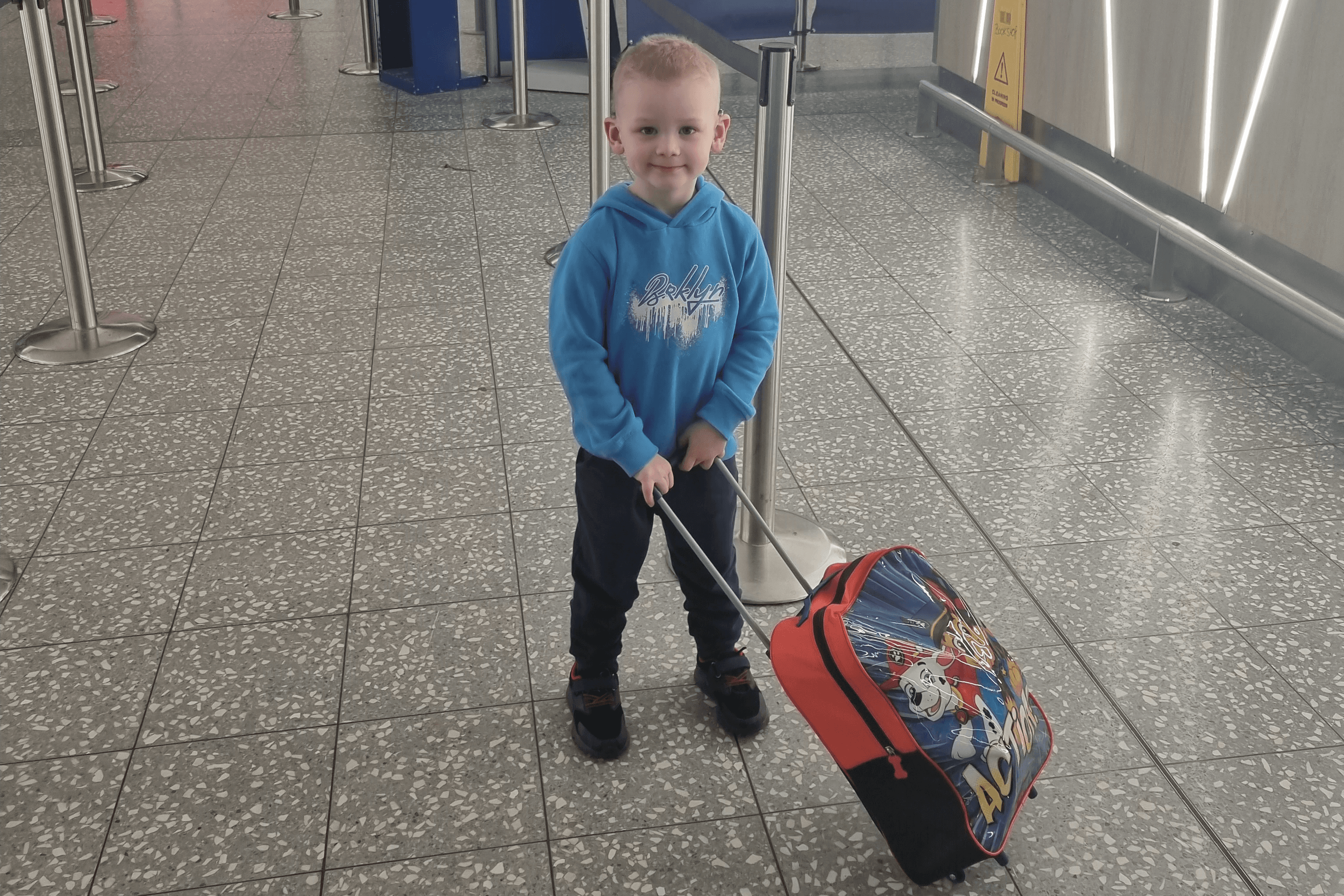 Young boy in an airport wheeling a suitcase