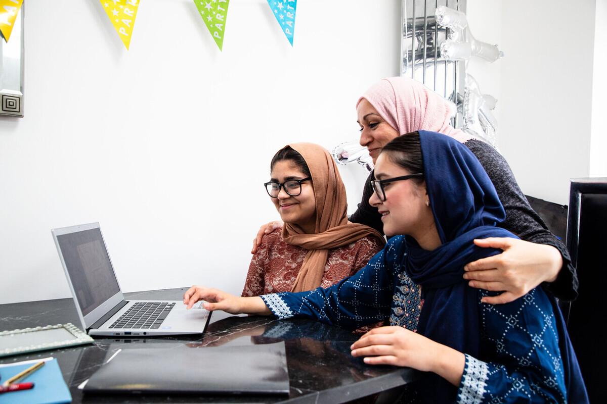 A mum and her two daughters look at a laptop together