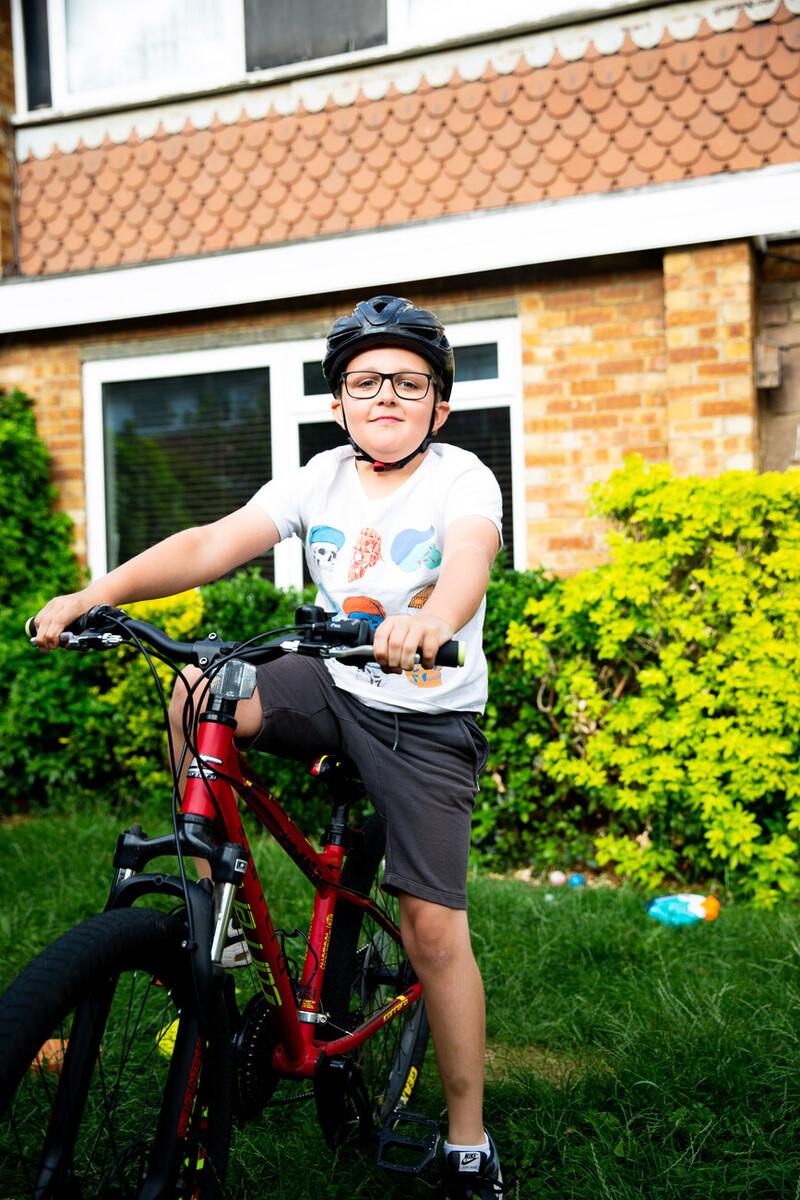 A young boy of about 10 is proudly sitting on his red bicycle. He is his garden and is wearing a black cycle helmet.
