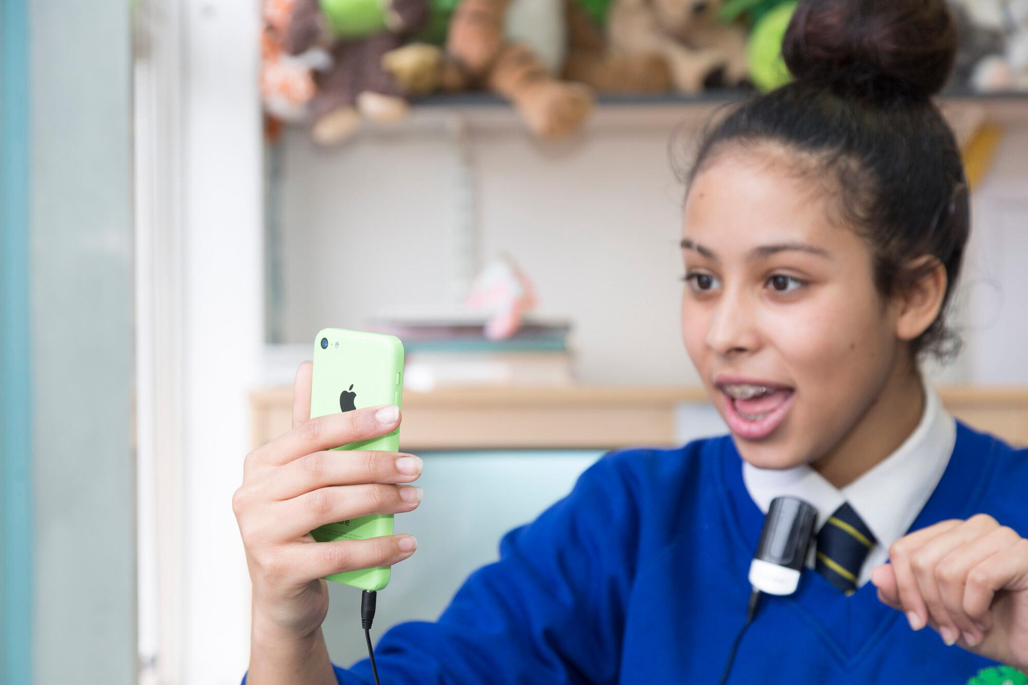 Secondary school girl holding a phone that is plugged into a streamer clipped onto her shirt collar