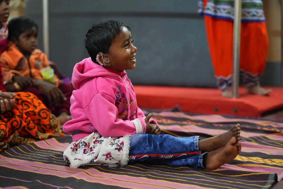 A smiling girl with hearing technology is sitting on the floor