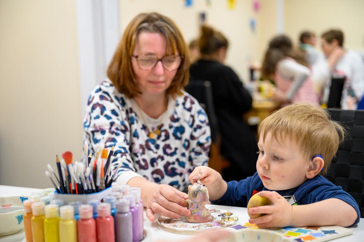 A young boy wearing hearing technology takes part in a craft activity, supported by a woman.