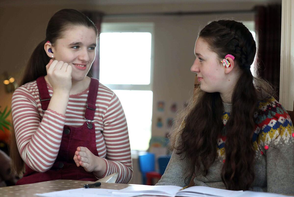 Two girls wearing hearing technology sign to each other