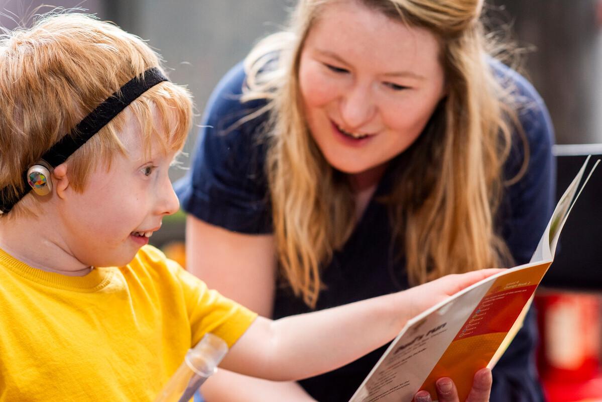 A young boy wearing hearing technology and a woman look at a book.