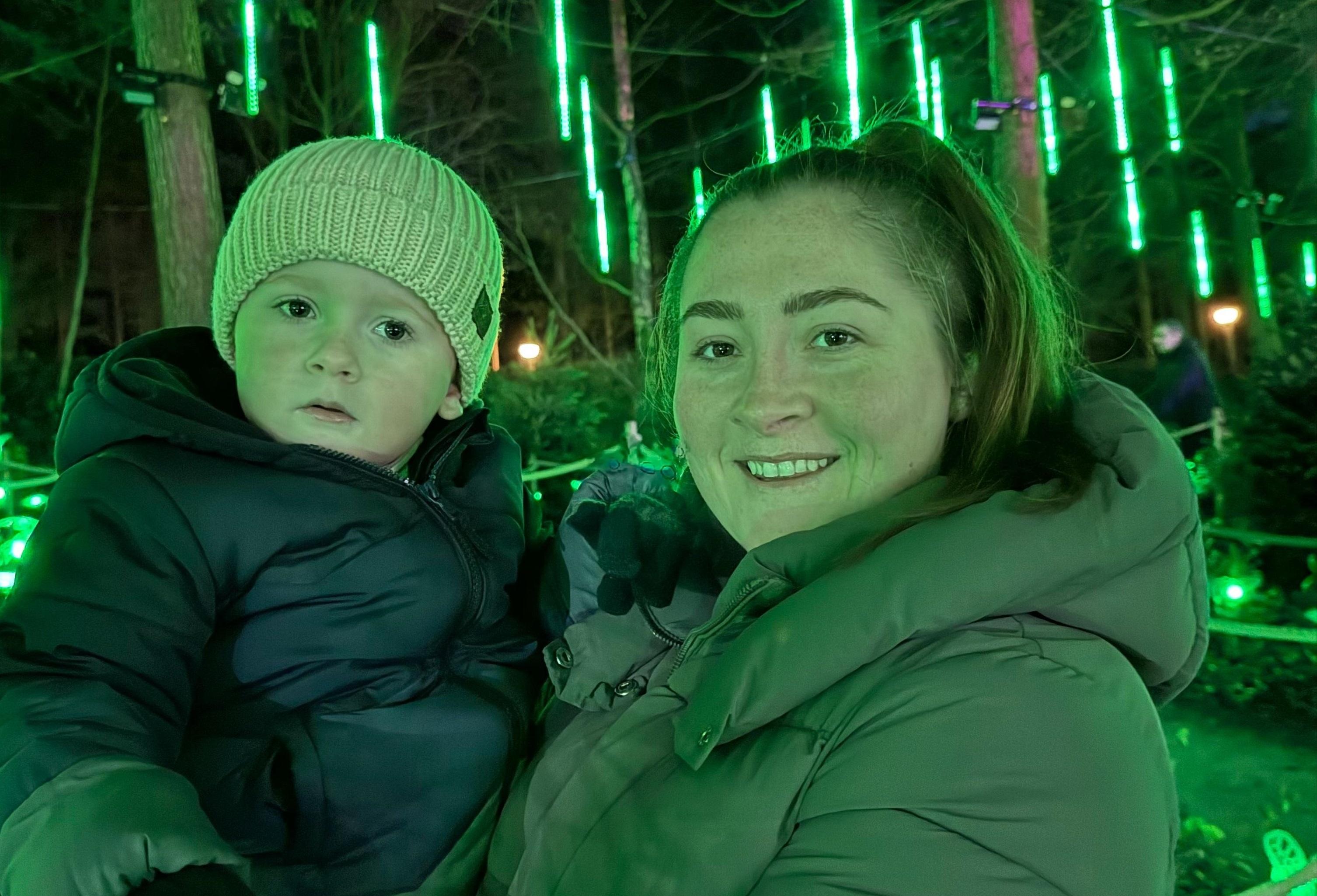 Louise holding George in her arms in a green lit woodland at night.