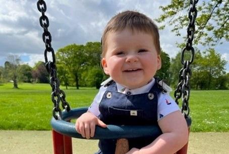 George smiling at the camera while sat in a swing at the park.