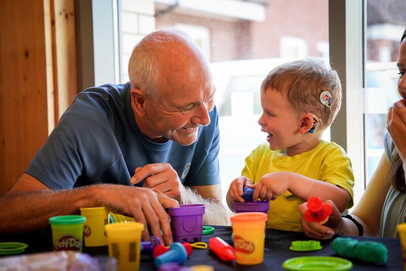 A man and deaf child are sat at a table playing with tubs of Play-Doh