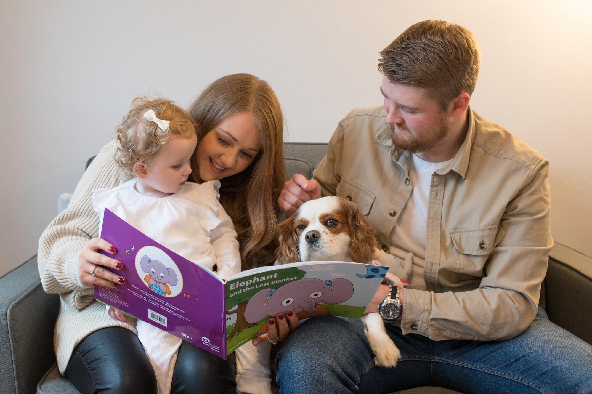 Mum, dad, baby daughter and dog reading 'Elephant and the Lost Blanket' together
