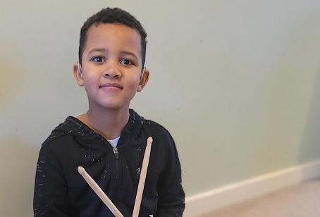 Isaac wearing his hearing aids and holding drum sticks crossed in front of him.