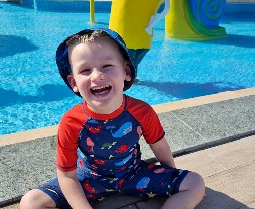 Kenzie wearing a swimsuit and hat smiling next to a swimming pool.
