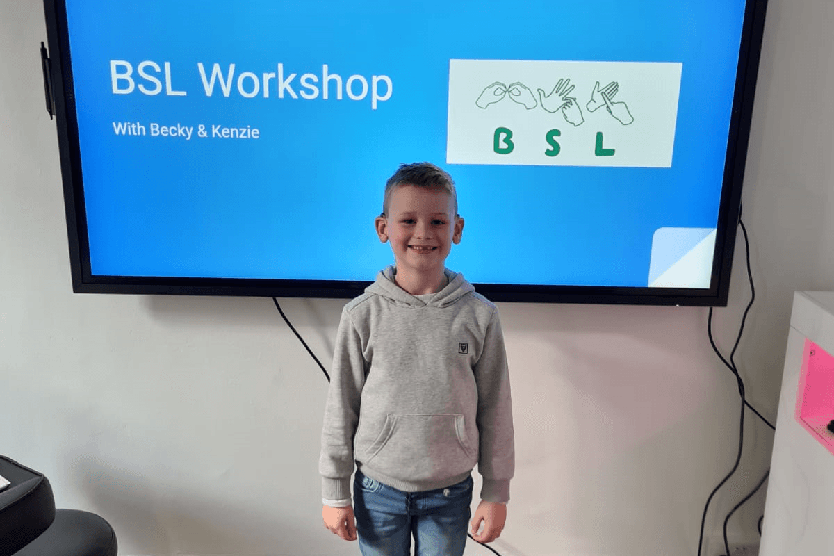 Young boy stands in front of a large PowerPoint screen that says 'BSL Workshop'